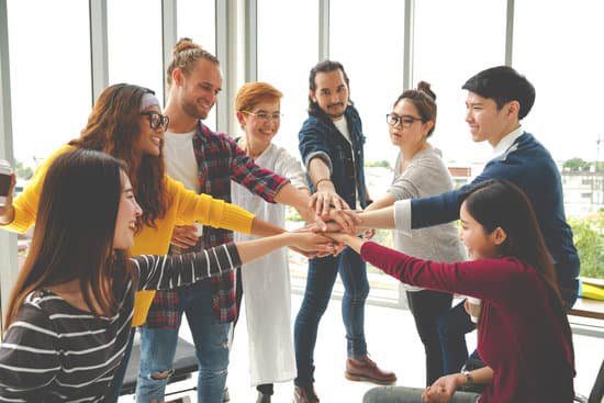 10 Best Team Building Activities For The Workplace Image of co-workers putting their hands together in the middle of a circle after team building activities for work, team building games, team building exercises.