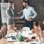 Image of a leader, supervisor, boss, manager shaking hands with individual in front of employees, subordinates, followers.