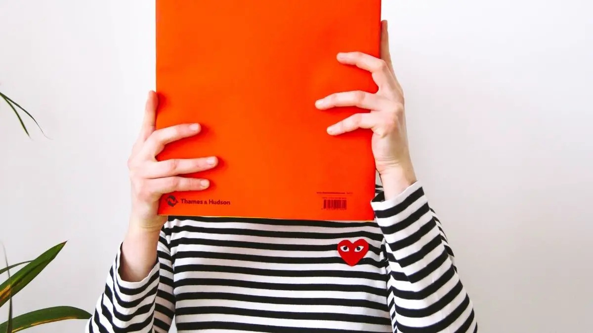 Image of a person hiding their face behind a folder.