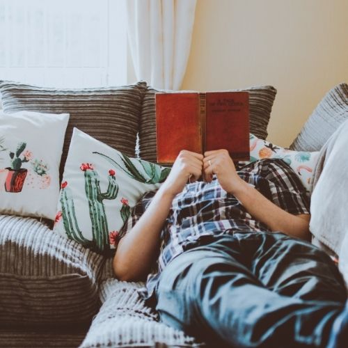 15 Signs of High Self-Esteem and How to Achieve It Person laying on the couch reading a book in their comfort zone.