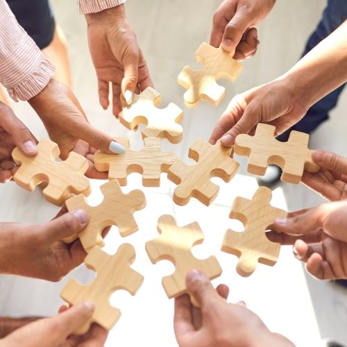 Fuel Team Success with These 30 Creative Morale Boosters Image of a team holding puzzle pieces for team building to boost morale on your team.