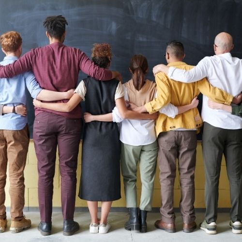 Image of people from different backgrounds, genders, religions, and other differences with their arms around each other. For why is diversity in the workplace important.