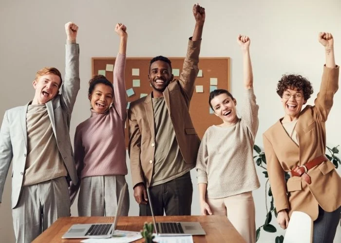 15 Group Facilitation Techniques and Tips to Kill Discussions People with smiles and their fists in the air in victory after a successful group facilitation.