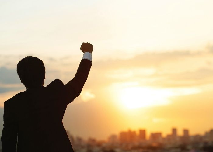 How To Have a Self-Motivated Personality Achieve Greater Success Man holding his hand in the air staring at a city off in the distance.