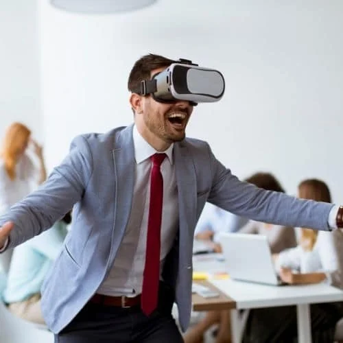 10 Fun Virtual Team Building Activities Employees Will Love Image of busniess man wearing VR goggles for challenges section in virtual team building activities and virtual icebreakers article.