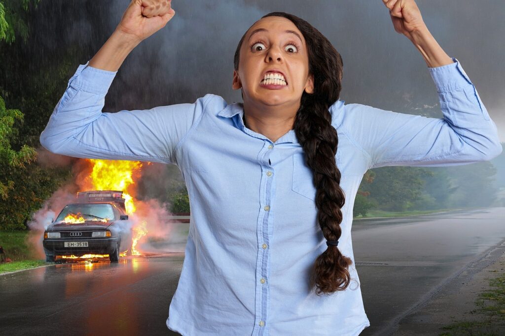 A lady very angry with her arms in the air and a car on flames behind her for the 3rd of the 7 stages of grief.