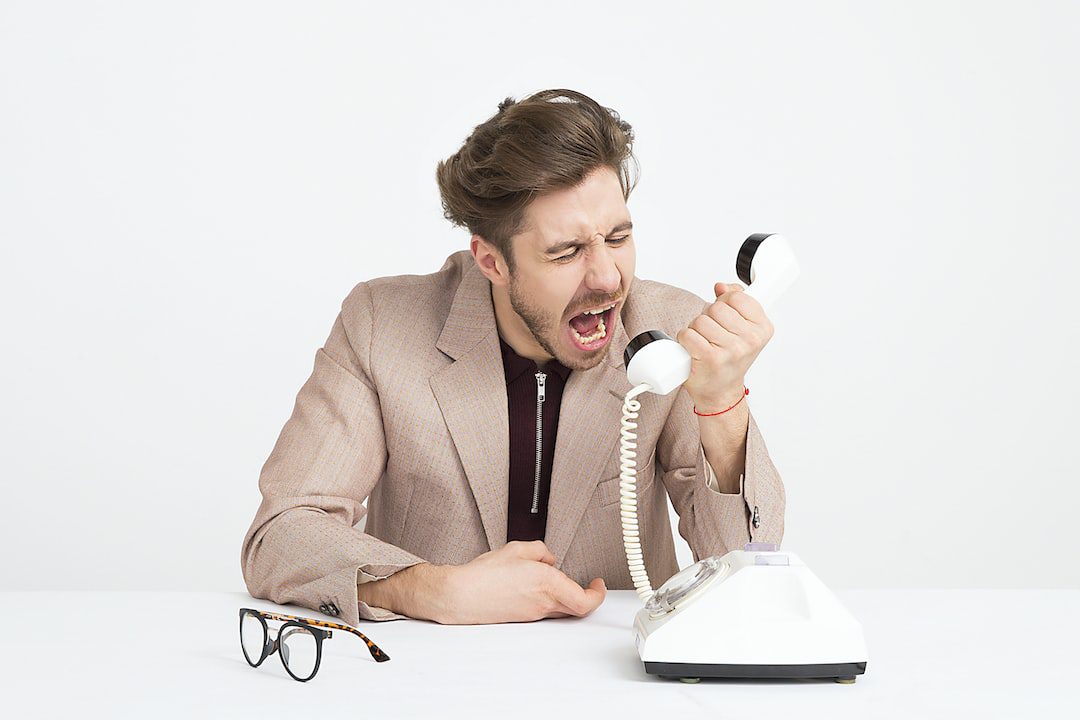 36 Crucial Tips for Improving Communication in the Workplace Person yelling into the receiver of a phone to show the wrong kind of communication in the workplace.