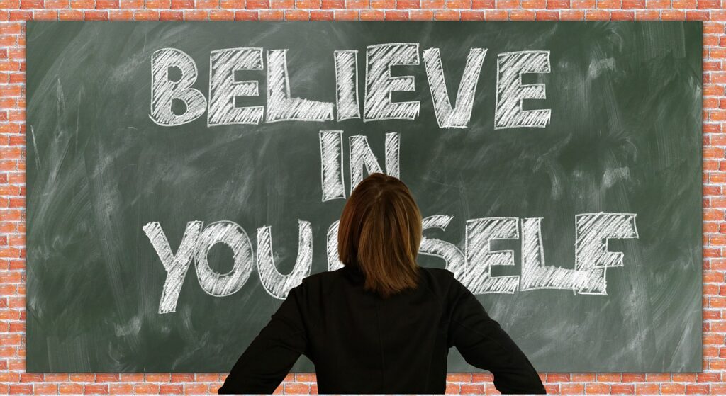 How to Maintain a Positive Attitude in the Workplace: 7 Critical Tips A person looking at a chalkboard with the words believe in yourself written on it for maintaining a positive attitude in the workplace.