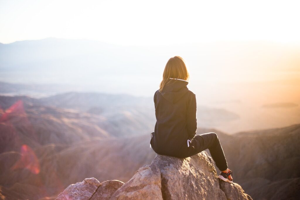 25 Crucial Keys To Success In Life You Can Start Now a woman sitting on a mountain thinking about the keys to success in life.